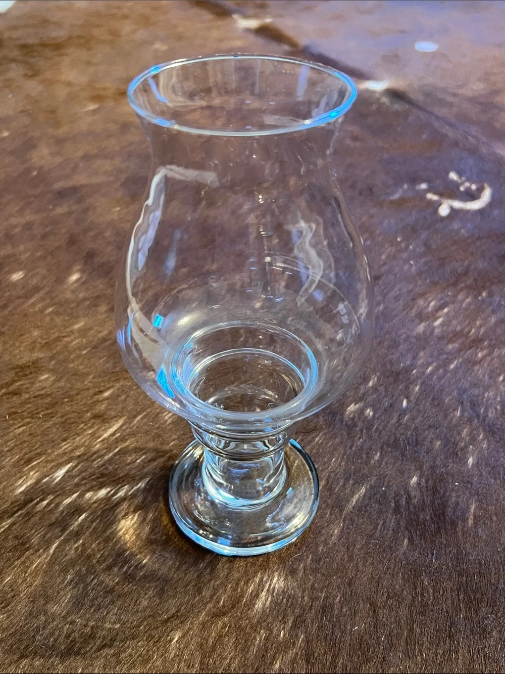 Clear glass hurricane candle holder features a pedestal base and a flared top